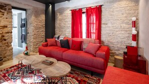 A modern living room with a red sofa, a patterned rug, and a stone wall. - Grande Bellezza - Renovated village houses designed like a hotel (ARS EN RE)
