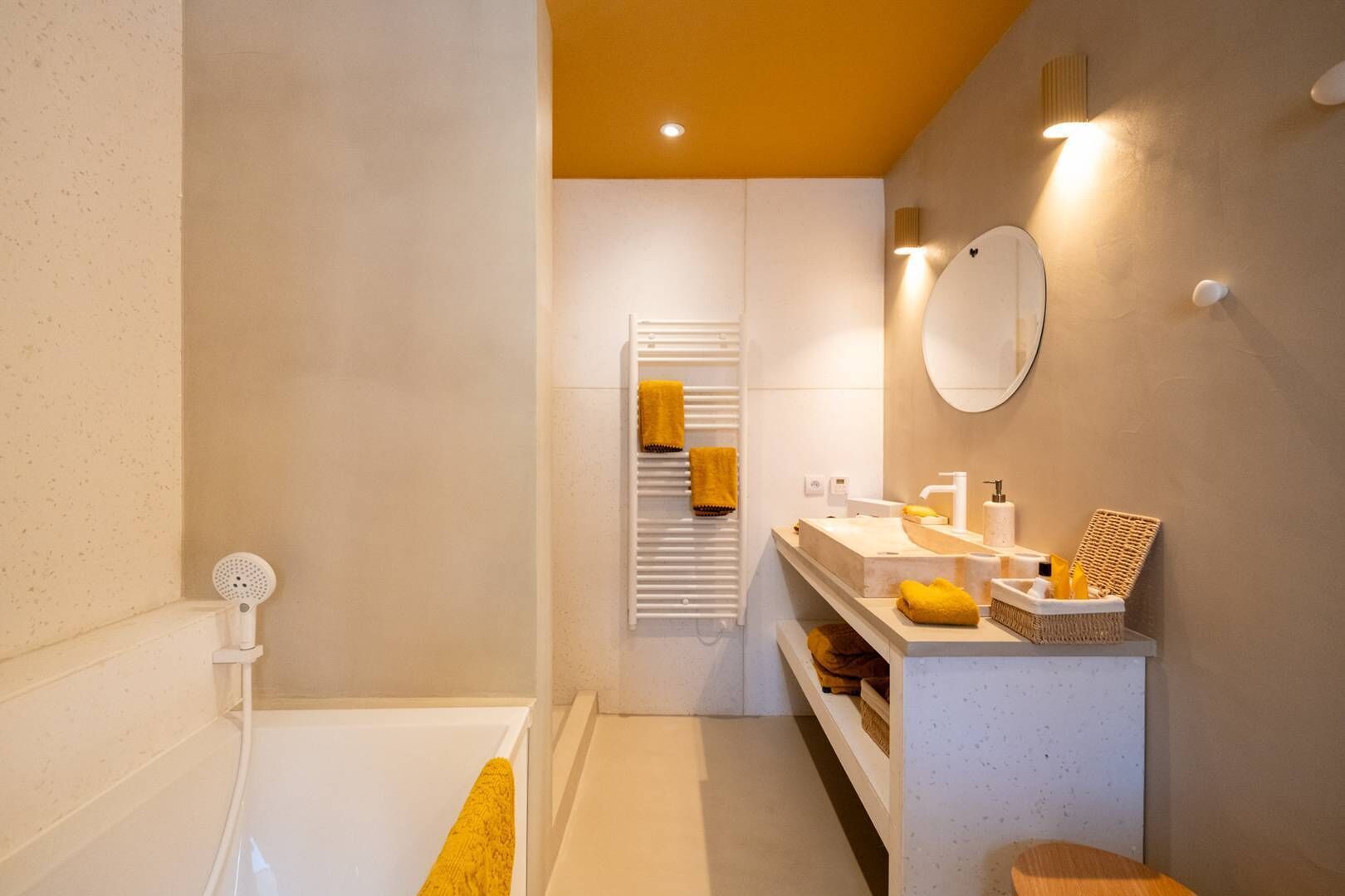 A modern bathroom with a bathtub, a white vanity with a mirror, and a towel rack with yellow towels.