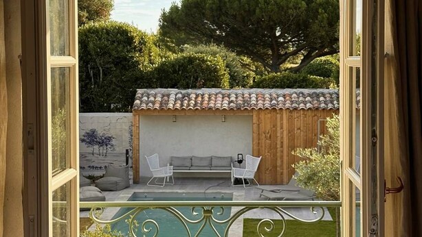 An open window with a view of a swimming pool, outdoor seating, and a building with a tiled roof. - Grande Bellezza - Renovated village houses designed like a hotel (ARS EN RE)