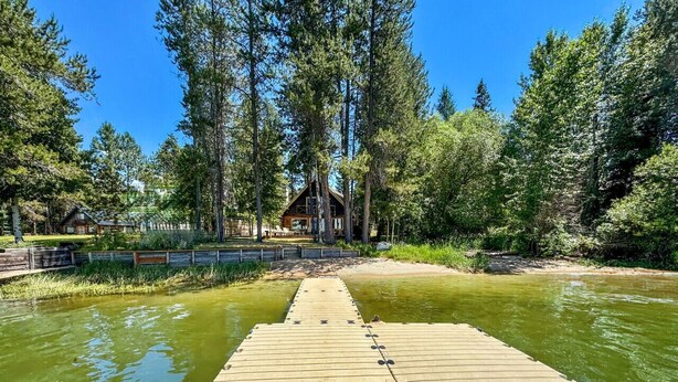 Eine Holzstege führt ins Wasser, umgeben von dichter Baumvegetation und einem kleinen Gebäude im Hintergrund.
