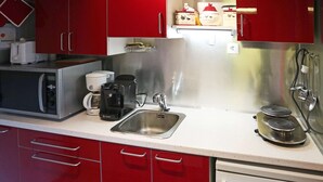 A modern kitchen with stainless steel appliances, red cabinets, and a white countertop. - Mini studio 2 persons located in the residence le belvédère (LES ORRES 1650)