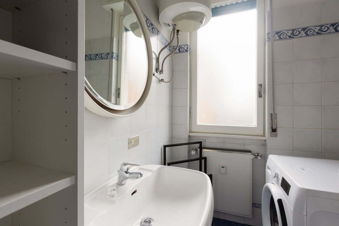 Un baño con lavamanos blanco, un espejo, una ventana y una lavadora.
