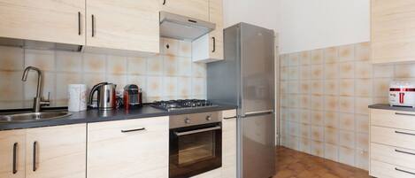 Una cocina con armarios de madera clara, un refrigerador de acero inoxidable, una estufa a gas y un horno empotrado.