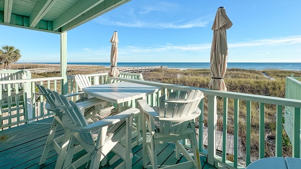 A covered outdoor area with a table and chairs, a wooden deck, and a view of the beach and ocean. - Sunkissed Sands @ Perdido Dunes | Spacious & Beachfront | Direct Beach Access | My Beach Getaways (Pensacola)