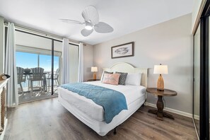 Un dormitorio con una cama grande, dos lámparas de noche, un ventilador de techo y vistas al exterior.