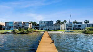Un muelle de madera que lleva a un hotel frente a la playa con varios balcones y palmeras.