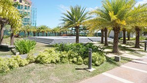 Een aangelegde tuin met palmboom en een betonnen bank, en een gebouw in aanbouw op de achtergrond.