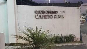Een bord met de tekst 'CONDOMINO CAMINO REAL' met een straatbeeld op de achtergrond.