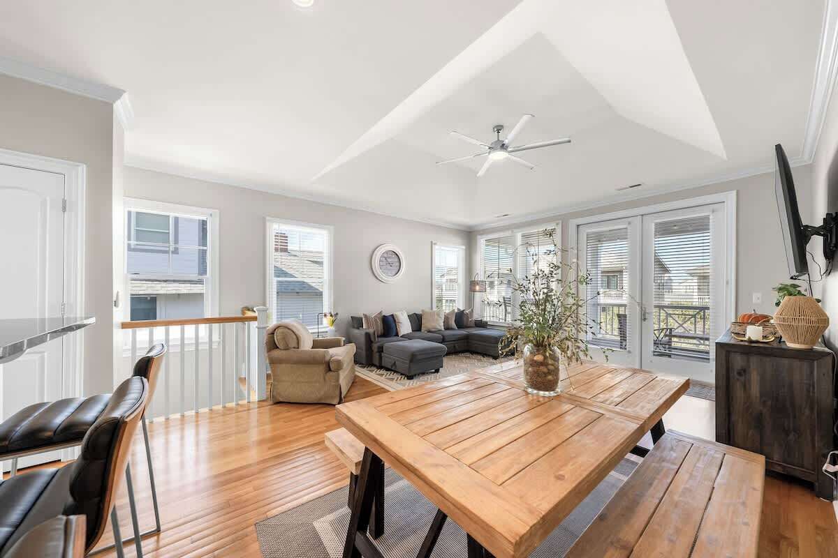 Un vaste espace de vie comprenant une table à manger en bois, un ensemble de canapés et un ventilateur de plafond.