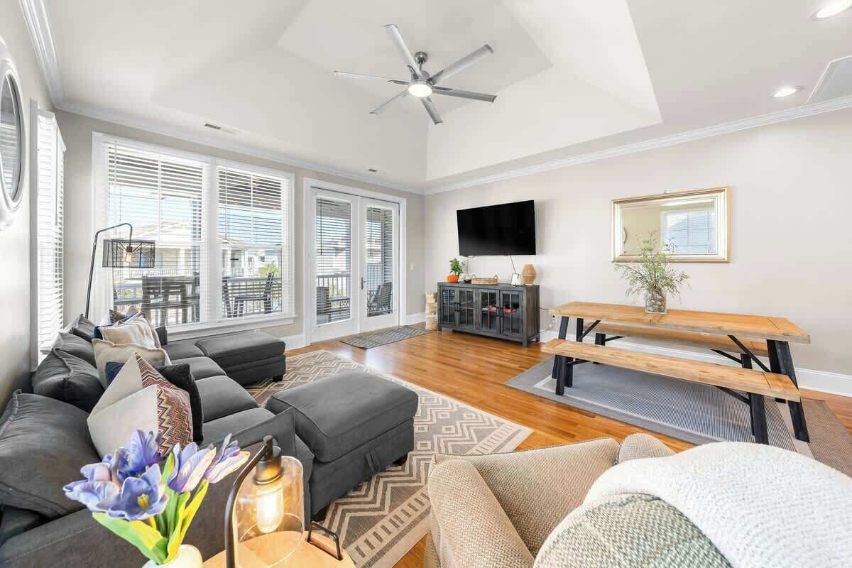 A spacious living room with a large sofa, a wooden dining table, and a ceiling fan.