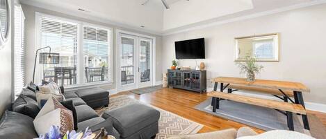A spacious living room with a large sofa, a wooden dining table, and a ceiling fan.