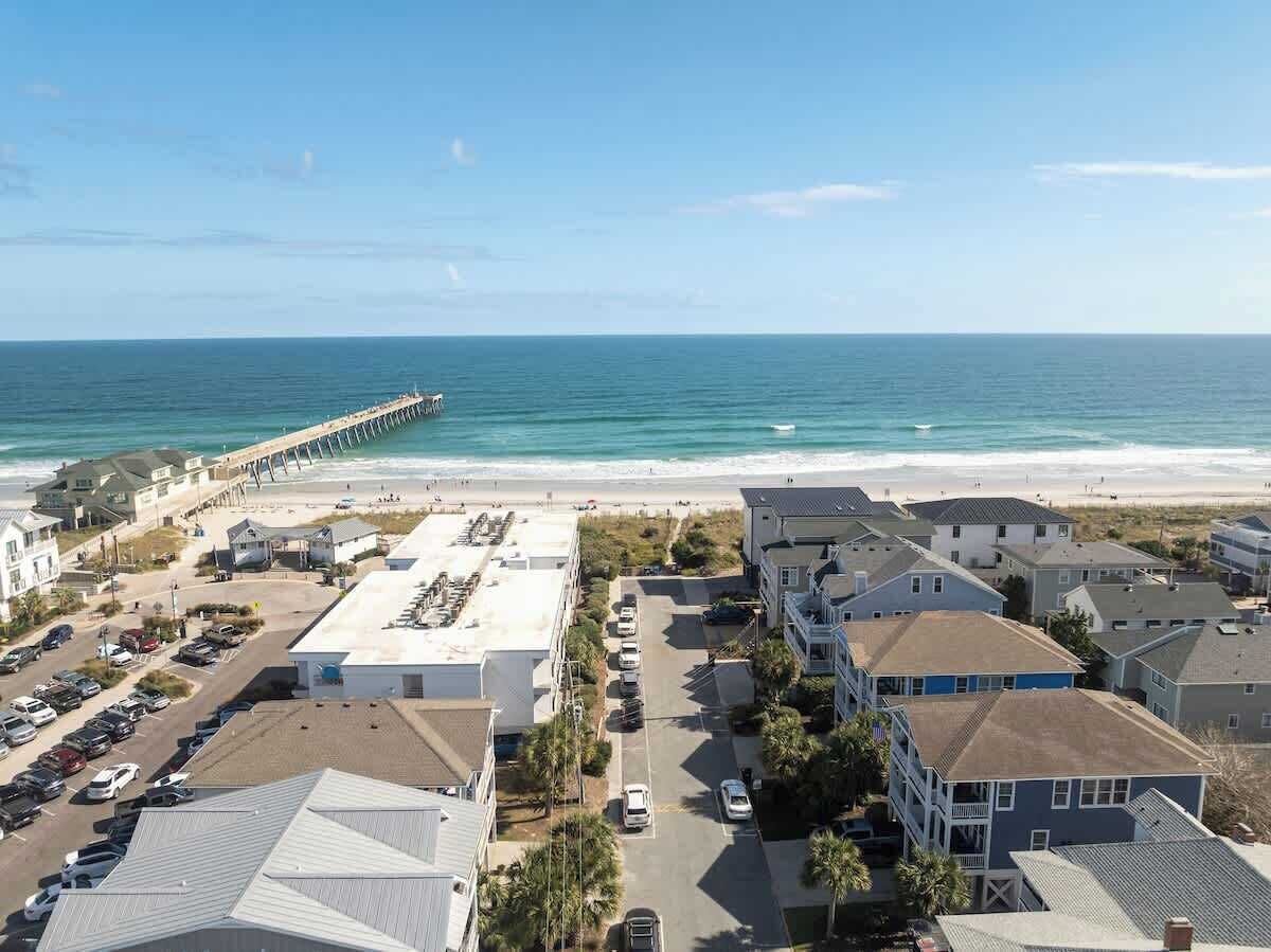 A coastal residential area with a pier extending into the ocean, houses with balconies, and a parking lot.