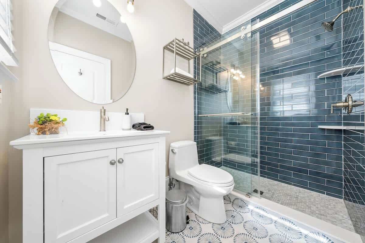 A bathroom with a white vanity, a toilet, a glass-enclosed shower, and a patterned floor.