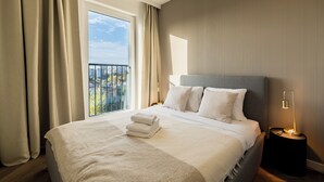 Habitación de hotel moderna con una cama grande, una mesita de noche y vistas de la ciudad desde un balcón.