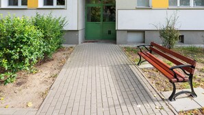 Een pad dat leidt naar een gebouw met een groene deur, een bankje en een kleine tuin.