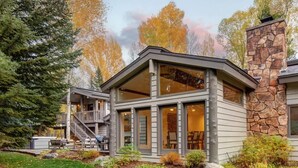 A modern house with a stone chimney, large windows, and a covered porch.