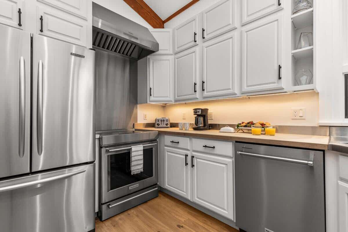 A modern kitchen with stainless steel appliances, white cabinetry, and a wooden ceiling.