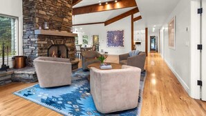 A spacious living area with a stone fireplace, wooden beams, and a blue patterned rug.