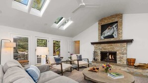 A spacious living room with a fireplace, comfortable seating, and skylights.