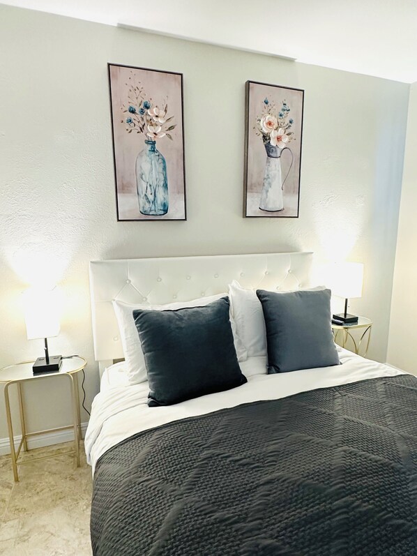 A neatly made bed with a white headboard, two bedside lamps, and two framed floral paintings on the wall.