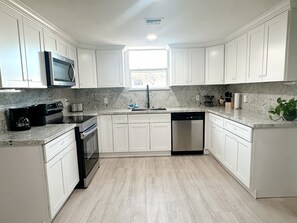A modern kitchen with white cabinets, a microwave, a coffee maker, and a dishwasher.