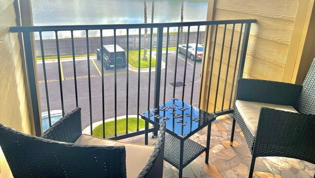 En balkon med et bord og stole, udsigt over en parkeringsplads og et vandareal.