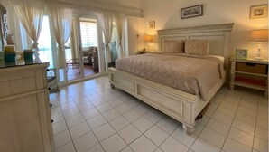 A bedroom with a large bed, a ceiling fan, a nightstand with a lamp, and a view of the outside through a window with curtains. - Stunning Caribbean Sea views! (Christiansted)