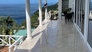A covered balcony with a view of the ocean, a tripod, and outdoor furniture. - Amazing mountain top home with stunning views! (Marigot Bay)