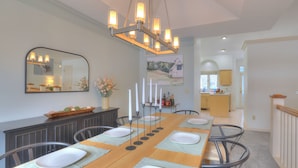 A dining area with a long table set for six, a chandelier, a mirror, and a painting on the wall. - Spacious 5-bedroom House, Hot Tub, Firepit, Game Rooms, Theater Room and More! (Decatur)