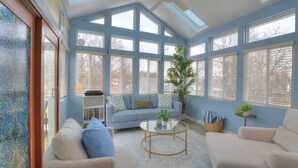 A sunroom with large windows, a sofa, a coffee table, and a potted plant. - Spacious 5-bedroom House, Hot Tub, Firepit, Game Rooms, Theater Room and More! (Decatur)
