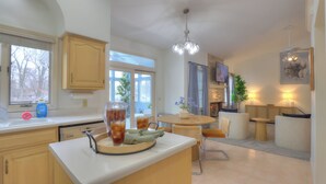 A modern kitchen with a central island, a dining area with a round table and chairs, and a living space with a sofa and a TV. - Spacious 5-bedroom House, Hot Tub, Firepit, Game Rooms, Theater Room and More! (Decatur)