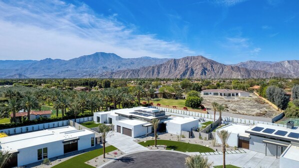 A modern building complex with multiple white structures, a central courtyard, and a mountain backdrop. - The Reserve at Polo Villas by AvantStay (La Quinta)