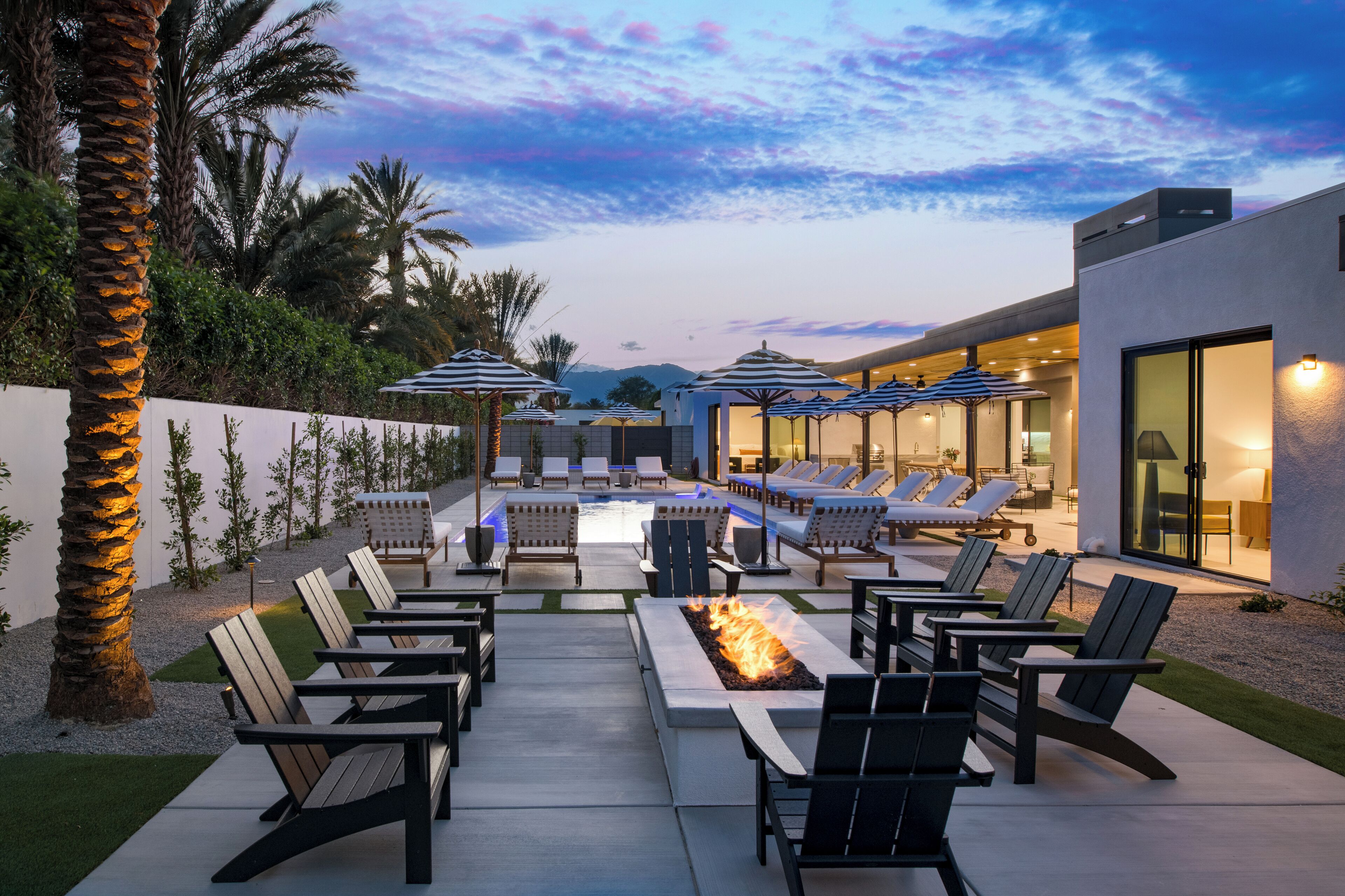 An outdoor lounge area with lounge chairs, a fire pit, and umbrellas.