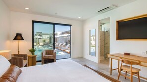 A modern hotel room with a large bed, a desk, a chair, a lamp, and a view of an outdoor pool area. - The Reserve at Polo Villas by AvantStay (La Quinta)