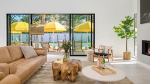 A modern living room with a leather sofa, wooden coffee table, and a view of the ocean through large glass doors. - The Reserve at Polo Villas by AvantStay (La Quinta)