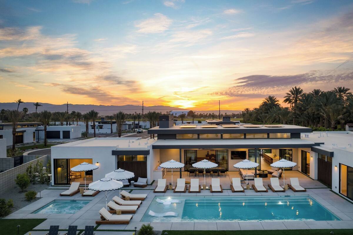 Ein modernes Haus mit Swimmingpool, Liegestühlen und Sonnenschirmen.