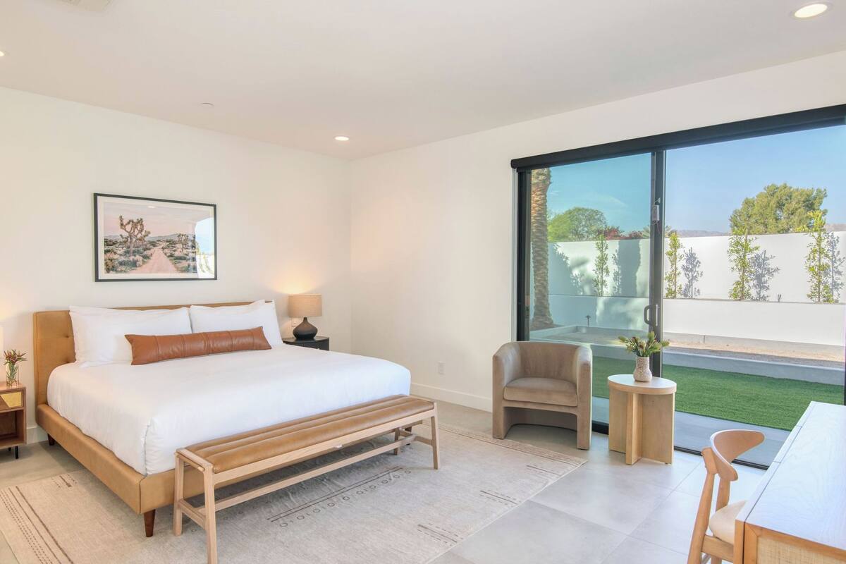 A modern bedroom with a large bed, bedside tables, a bench, a chair, and a view of the outdoors.