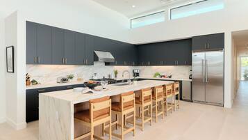 A modern kitchen with dark cabinets, a large island with bar stools, a stainless steel refrigerator, and a skylight.