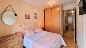 Een slaapkamer met een bed, nachtkastjes, een spiegel, kunstwerken, een kledingkast en een televisie.