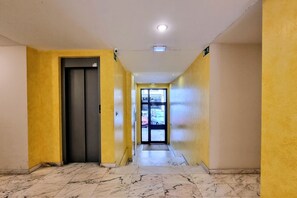 A hallway with yellow walls, a marble floor, and a door leading to a parking area. - La Folixa Apartment (Posada De Llanes)