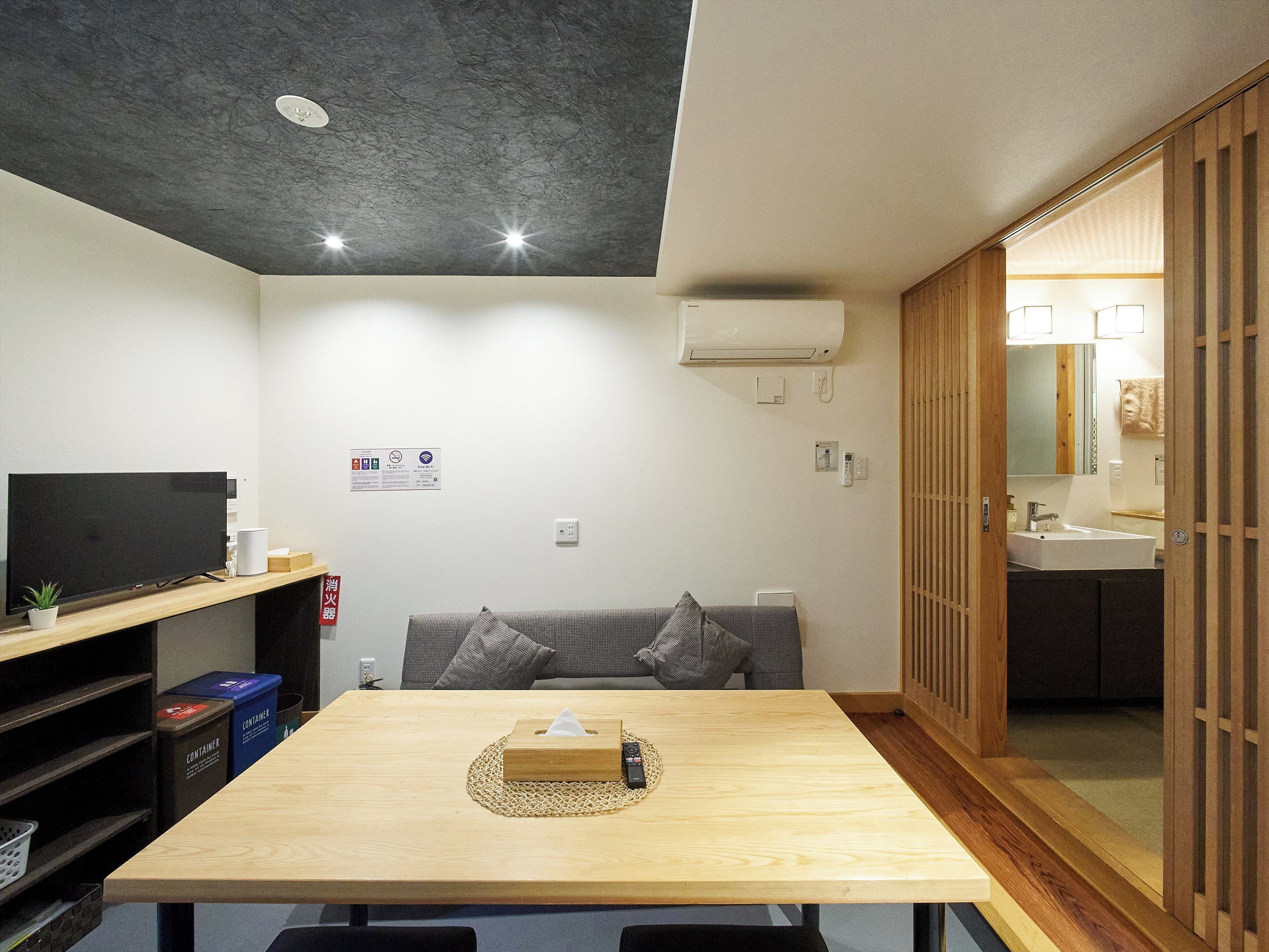 A modern living room with a wooden table, a sofa, a TV, and a sliding door leading to a bathroom.