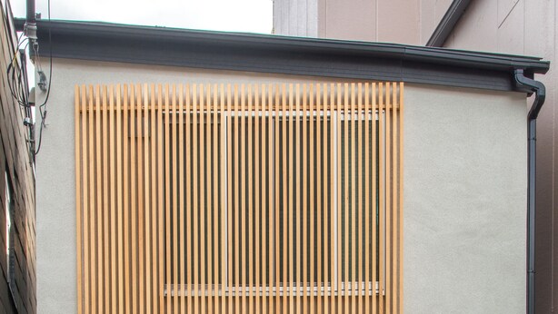 Un bâtiment moderne doté d’une façade à lattes de bois, d’une porte centrale et d’un petit espace extérieur agrémenté de plantes.