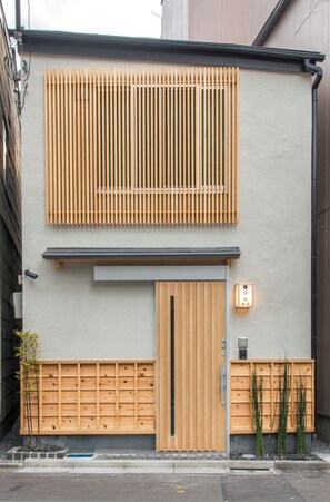 Un edificio moderno con fachada de listones de madera, una puerta central y un pequeño espacio exterior con plantas.