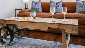 A wooden table with two glasses of white wine, a small potted plant, and a candle holder. - The Corral | 2/1, Hot Tub, Full Kitchen, Gas Grill, Gazebo (Fredericksburg)