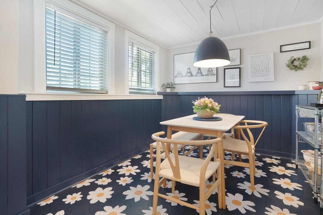 Et spiseområde med et bord og stole, en hængende lampe samt en væg med billeder og en krans.