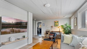 A modern living room with a large painting, a wooden coffee table, a gray sofa, and a dining area. - Stylish Downtown Cottage, Walk Everywhere (Bend)