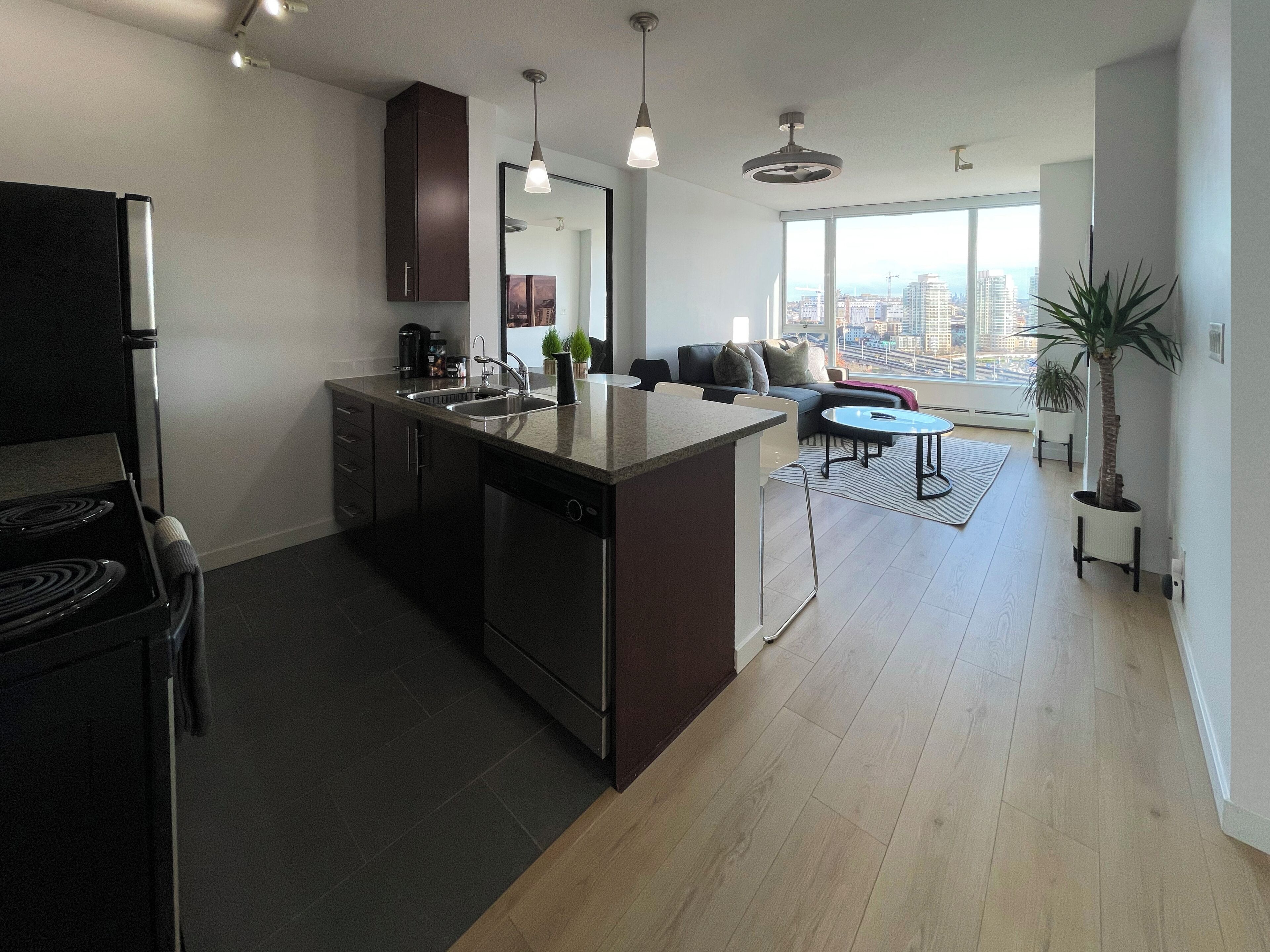 A modern kitchen with a central island, a dining area with a round table, and a large window offering a city view.