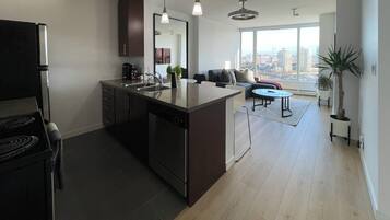 A modern kitchen with a central island, a dining area with a round table, and a large window offering a city view.