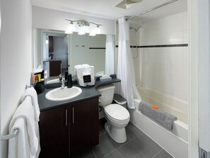 A modern bathroom with a sink, toilet, and shower. There are towels and toiletries on the counter.