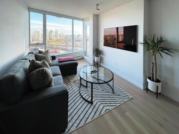 A modern living room with a large window, a sofa, a coffee table, and a potted plant.